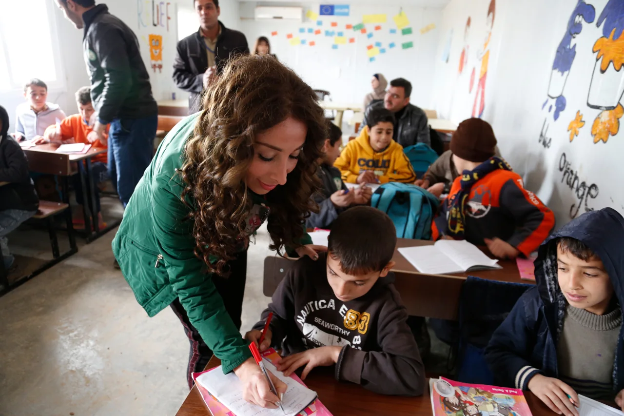 A teacher helps a student in a school in Zaatari
